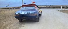 an old police car parked on the side of a dirt road next to a field