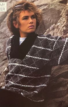 a woman wearing a black and white knitted sweater sitting on top of a rock