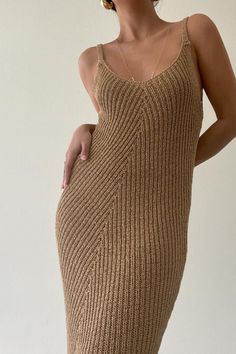 a woman in a tan knitted dress posing with her hands on her hips and looking off to the side