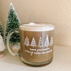 a coffee mug sitting on top of a table next to small trees and a christmas tree