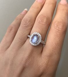 "A lovely Halo Setting featuring an oval shaped cabochon Rainbow Moonstone embellished with pave set cubic zirconia handcrafted in Sterling Silver. Wrapped in a box ready for gift-giving.(R-egt-47) Ring Info ---------------------- Moonstone measure 9mm x 7mm Moonstone with Halo measure 13mm x 11mm Ring Shank Width 2mm Model ring size 5 ----> Please note there is an additional fee, if we have to size the ring again so please make sure you know your ring size. ---> Don't know your ring size? Oval Moonstone Ring In White Gold, Elegant Opal Ring With Oval Cabochon And Accent Stones, Elegant Oval Cabochon Opal Ring With Accent Stones, White Gold Oval Opal Ring, Anniversary Sterling Silver Moonstone Ring With Gemstone Accents, Anniversary Moonstone Ring With Diamond Accents, Oval Cabochon Birthstone Promise Ring, Oval Moonstone Ring For Gift, Anniversary Moonstone Ring With Oval Cabochon