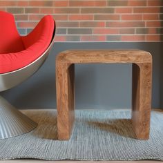 a red chair sitting next to a wooden table in front of a brick wall and floor