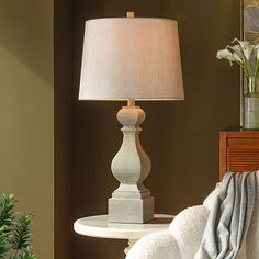 a white table lamp sitting on top of a wooden table next to a mirror and potted plant