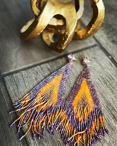 a pair of yellow and purple earrings sitting on top of a wooden table next to a gold ring