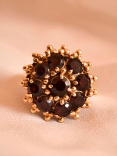 This big, bold, statement ring will enter the room before you do; fashioned in nicely toned 14kt yellow gold, it is crafted with a large, circular setting embellished with stunning beaded trios all around the circumference, creating a very bohemian granulated aesthetic. It is stunningly set with 9 glittering garnet stones, deeply wine coloured, catching the sunlight so strikingly. The garnets all bear moderate to heavy inclusions, lending them such a moody, mysterious presence that will mesmeriz Garnet Stone, Wine Colored, Vintage Bohemian, Cluster Ring, Statement Ring, Rings Statement, Unique Rings, Favorite Jewelry, Statement Rings