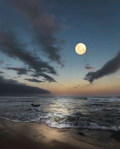 the moon is setting over the ocean with waves coming in to shore and dark clouds