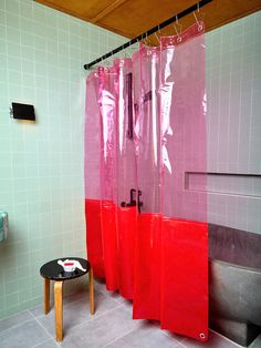 a bathroom with pink and red shower curtains next to a black stool in front of the tub