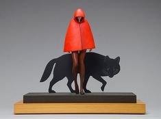 a statue of a woman with a red coat and black cat on a wooden base