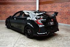 the rear end of a black sports car parked in a parking garage next to a brick wall