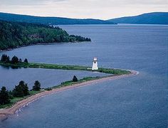 an island with a light house on it in the middle of water surrounded by trees