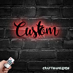 a person holding a cell phone in front of a brick wall with the word custom on it