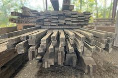 many pieces of wood are stacked together in the middle of a pile, with trees in the background