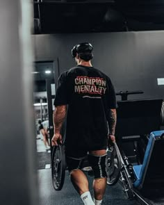 a man in black shirt and knee braces holding a pair of exercise equipment while walking through a gym