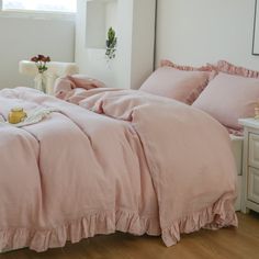 a bed with pink sheets and pillows in a white room next to a window,