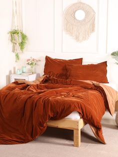 a bed with orange sheets and pillows in a room next to a wall hanging on the wall