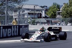 a man driving a racing car down a race track with people watching from the sidelines