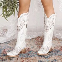 a close up of a person wearing white cowboy boots and holding a bridal bouquet