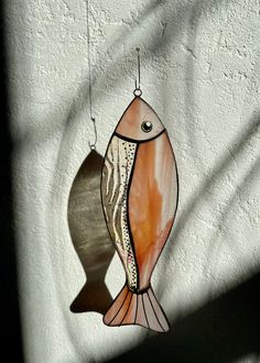 a glass fish hanging on the side of a wall next to a shadow cast by a window