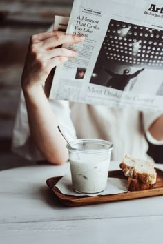 a person sitting at a table reading a newspaper and eating bread with a glass of milk