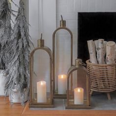 three lit candles sitting on top of a wooden table next to a basket filled with logs