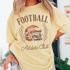 Gear up for game day with our Football Athletic Club Comfort Color Tee. Crafted for comfort and style, this tee is perfect for fans who want to show their support in a laid-back yet spirited way. Emblazoned with the emblem of our Football Athletic Club, this tee exudes team spirit and camaraderie. Whether you're cheering from the stands or watching from home, our tee ensures you'll be representing your team in style. Made from premium materials, this tee offers unparalleled comfort and durabilit College Baseball Season Screen Print Tops, Sporty Top With Team Logo For Sports Season, Sports Fan Tops With Team Logo For Game Day, Casual Tops With Team Logo For Game Day, Casual Top With Team Logo For Baseball Season, Casual Tops For Baseball Season Fan Gear, Football Season Tops With Team Logo For Sports Fans, Sports Fan Tops With Team Logo For Football Season, Sports Fan Tops With Team Logo For Baseball Season