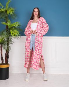 a woman standing in front of a blue wall wearing a pink and white cardigan