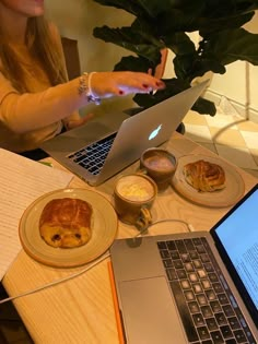 a laptop computer sitting on top of a wooden table next to a plate of food