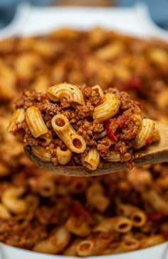 a wooden spoon filled with pasta and ground beef on top of a white dish full of noodles