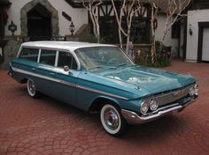 an old blue and white station wagon parked in front of a house with brick driveway