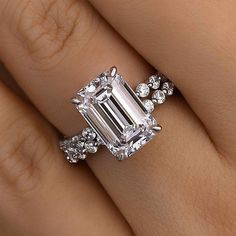 a woman's engagement ring with an emerald cut diamond surrounded by small white diamonds