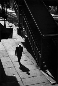 a person walking down a sidewalk next to a ramp and stairs in black and white