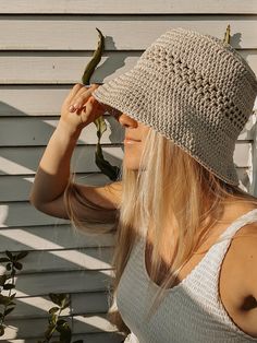 a woman wearing a crocheted hat and holding a plant in front of her face