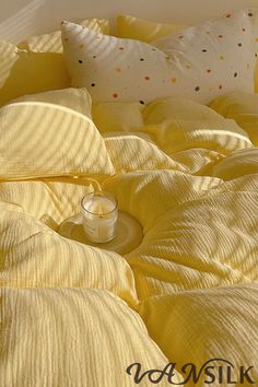 a bed with yellow sheets and pillows on top of it, next to a candle