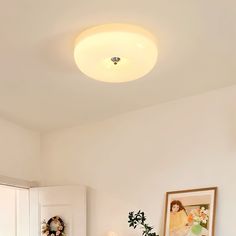 a bedroom with white walls and wooden flooring has a round light fixture above the bed