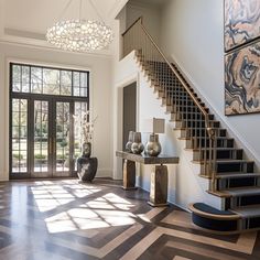 an elegant entryway with wood floors and chandelier above the stairs is flanked by two vases