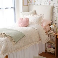 a bed with pink and green pillows on top of it next to a white headboard