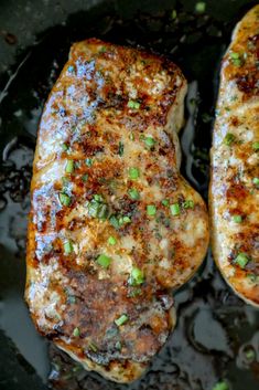 two pieces of meat with green onions on top in a frying pan, ready to be cooked