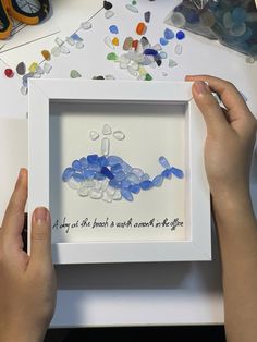 two hands are holding a framed artwork with blue and white sea glass in the shape of a woman's body