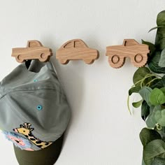 two wooden cars hang on the wall next to a green hat and potted plant