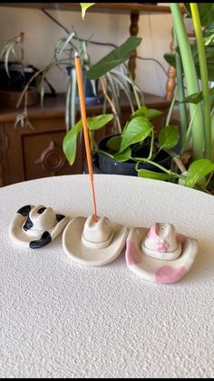 three small ceramic animals sitting on top of a white table next to a potted plant