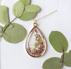 "A beautiful and unique Botanical inspired terrarium necklace with gorgeous real pressed Yorkshire Heather picked on the moors, gorgeous white and pink gypsophila and folliage.   Beautiful lilac flowers in a teardrop pendant.  For someone who needs to wish, for wishes to be granted and for communicating with the spirit world.  The flower is encapsulated in a crystal clear Resin which is Non-toxic, No VOCs, No fumes, No solvents, Non-flammable, Non-hazardous, No BPA.  The necklace chain is gold plated solid brass or stamped 14k gold filled chain as shown in last photo. This chain is much more long lasting and delicate.  The pendant is 1 inch in width and length.  A cute and eco friendly gift for yourself or a loved one. 🌼 So someone you love can bring spring with them wherever they go 🌼 Nature-inspired Rose Gold Necklace, Bohemian Jewelry As A Gift Featuring Birth Flower, Delicate Rose Gold Keepsake Jewelry, Nature-inspired Rose Gold Pendant Necklace, Bohemian Gold Keepsake Jewelry, Rose Gold Birth Flower Jewelry Keepsake, Handmade Yellow Gold Keepsake Jewelry, Nature-inspired Necklace With Adjustable Chain For Gift, Nature-inspired Jewelry With Adjustable Chain As Gift