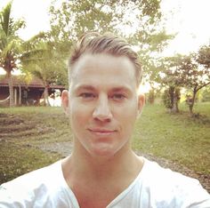 a man in a white shirt is posing for a photo with trees and grass behind him