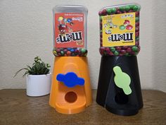 two gummy machines sitting next to each other on top of a wooden table near a potted plant