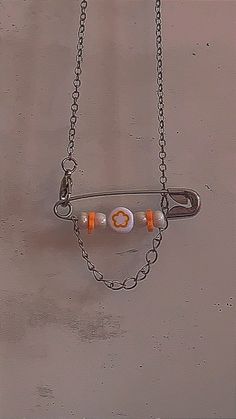 an orange and white necklace hanging from a chain on a gray wall with the word love spelled in small letters