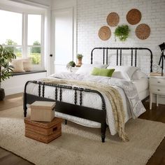 a bedroom with white brick walls and black iron bed frame, green throw pillows on the floor