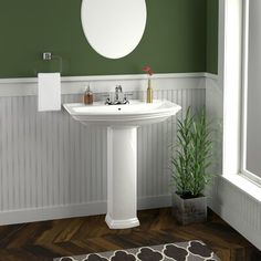 a white pedestal sink in a bathroom with green walls and wood flooring next to a potted plant