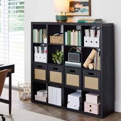 a black bookcase filled with lots of books next to a desk and chair in front of a window