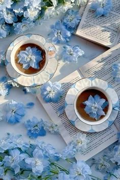 two cups of tea with blue flowers on them and an open book in the middle