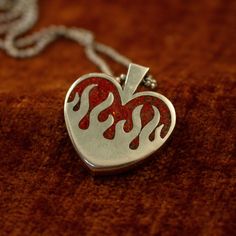 The silver hearts on fire pendant features a chunky design and a stunning ruby red opal inlay (or your chosen stone). Alternatively, you can opt for a transparent pendant without any inlay. It boasts a substantial 4 mm thickness and stands 26 mm tall. PLEASE READ: The production and delivery of your piece may take anywhere from 2-4 weeks as it is custom made by a real person. Grit Trade Co. is a curated collection of unique sterling silver jewelry inspired by American culture, music, and motorcy