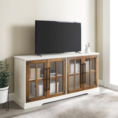 a flat screen tv sitting on top of a white entertainment center next to a potted plant